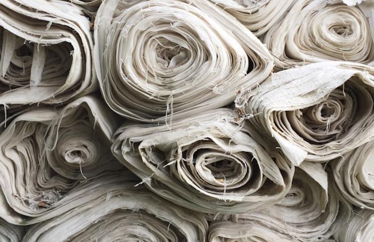 The image shows a stack of rolled fabric in neutral tones.