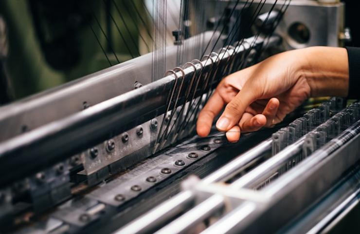 A hand is adjusting the threading on a textile loom.