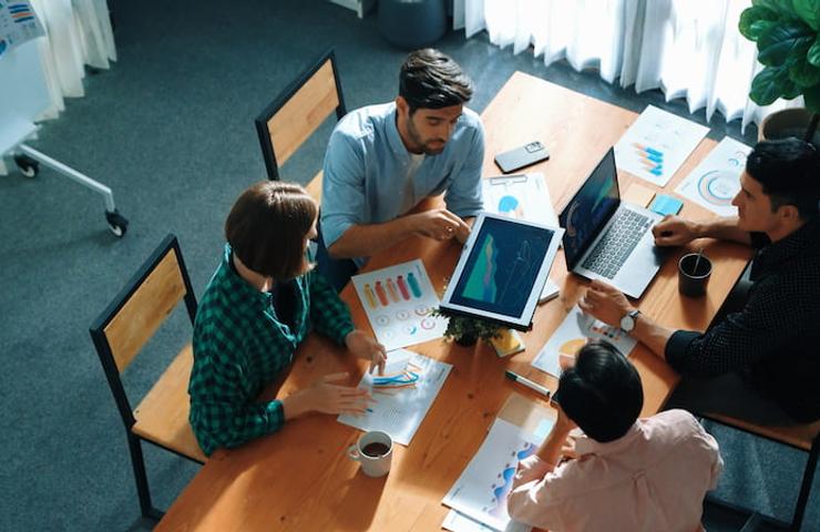 A group of four people engaging in a business meeting around a table with laptops and documents.