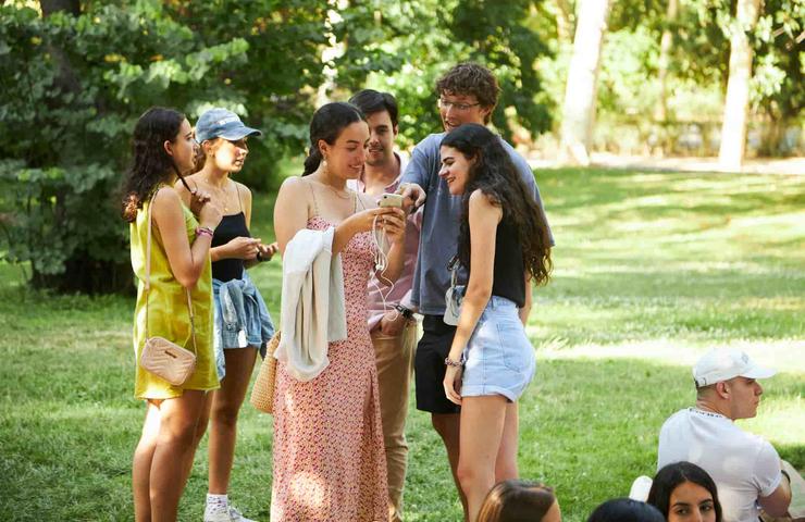 A group of young people standing together in a park, chatting and smiling during a sunny day.