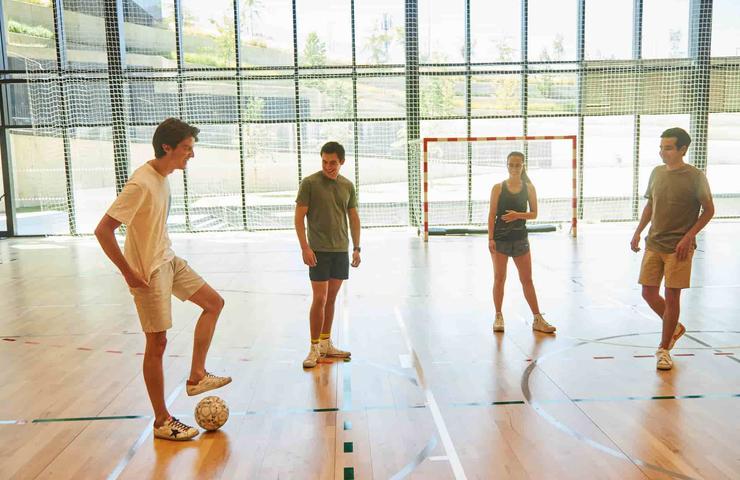 Four young adults are standing in an indoor sports court, preparing to play soccer.