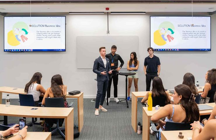 A group of students presents a business idea in a modern classroom while others listen.