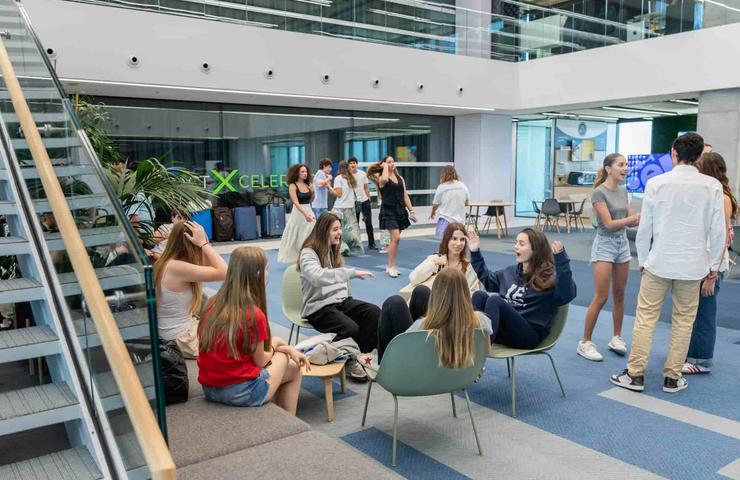 Groups of young people chatting and relaxing in a modern office lobby with large windows.