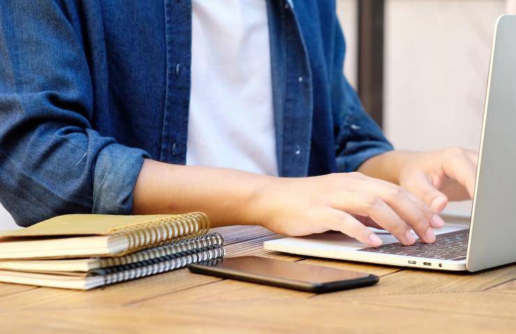 A person working on a laptop with notebooks and a smartphone on the table