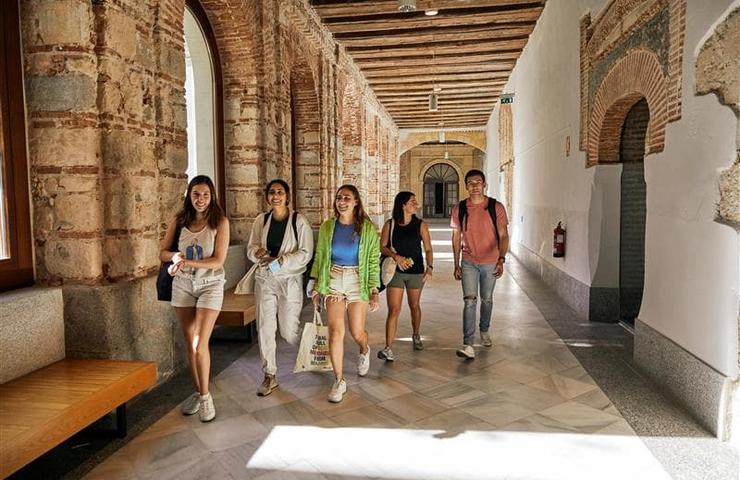 A group of young people happily walking through a historical corridor with arches and exposed brick walls.