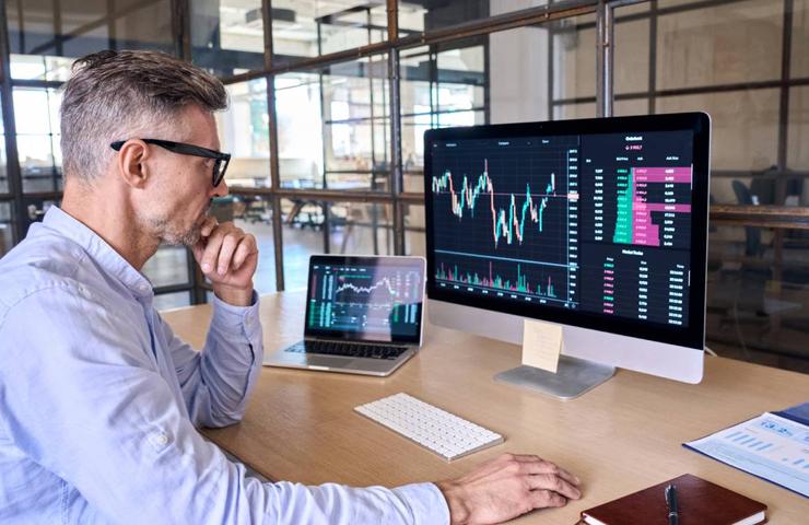 A man analyzing financial data on multiple computer screens in a modern office setting.