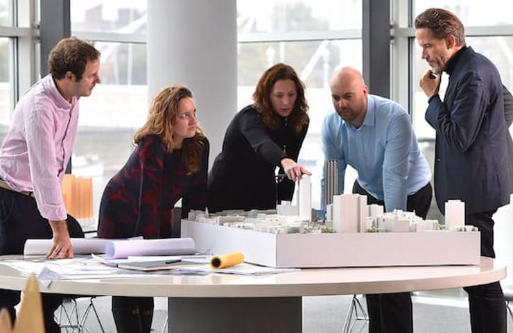 A group of five professionals discussing over a scale model of a city in a modern office.