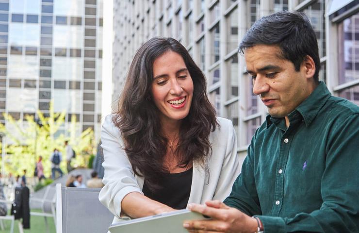A woman is joyfully showing something on a tablet to a man in a modern outdoor setting.