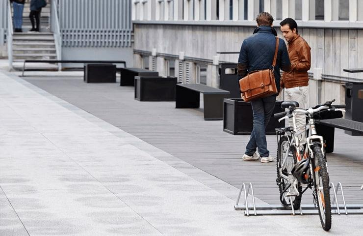 Two men talking beside a parked bicycle on an urban walkway.