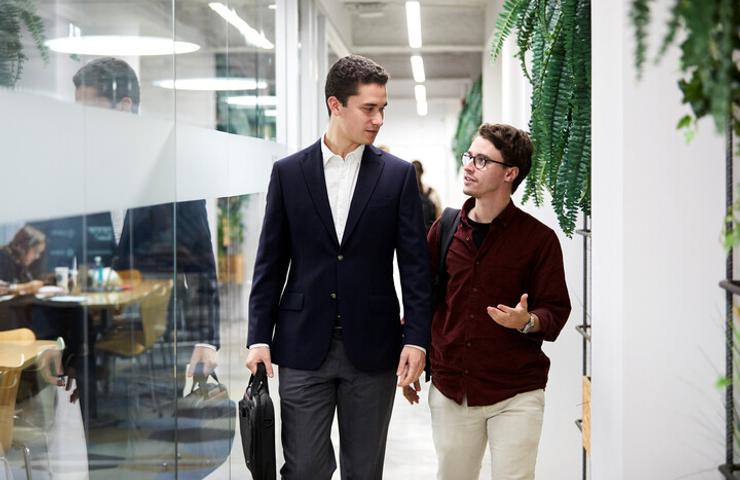 Two men walking and talking in a modern office corridor.