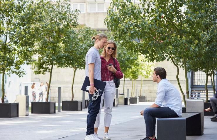 Three young people are engaged in a conversation in a modern urban park setting.