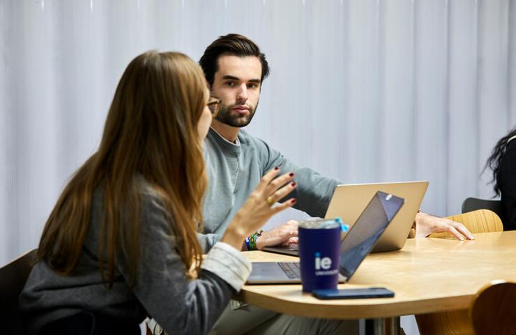 A man and a woman discussing over a laptop at a table in a modern office.