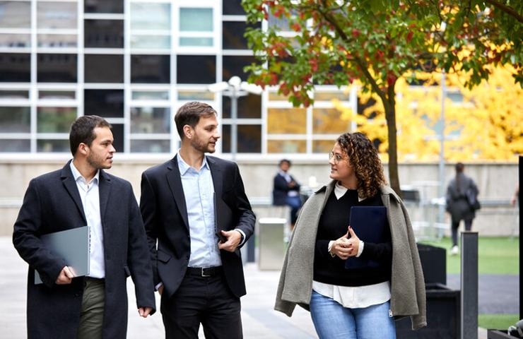 Three business professionals walking and talking outside a modern office building.