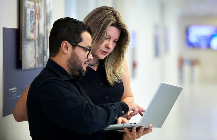 Two colleagues are discussing work while looking at a laptop screen.