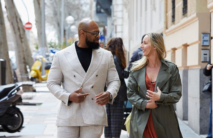 A man and a woman are walking together on a city street, engaged in conversation.