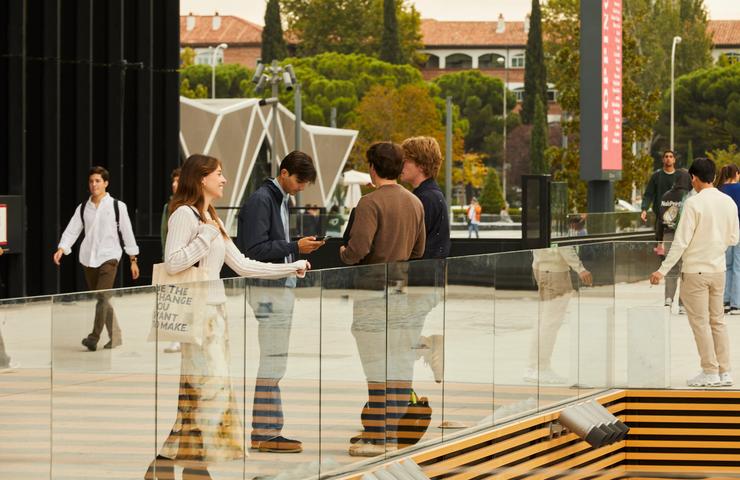 People are conversing and walking in a modern outdoor plaza.