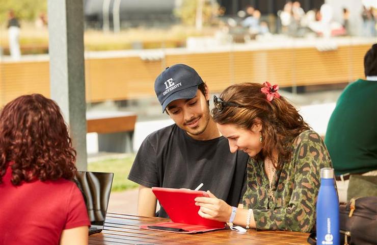 Two young adults studying and discussing notes together at an outdoor table.