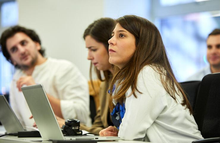 A group of young adults attentively participates in a meeting or a workshop in a modern office setting.