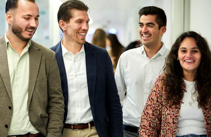 Four colleagues, two men and two women, are walking happily together in an office corridor.