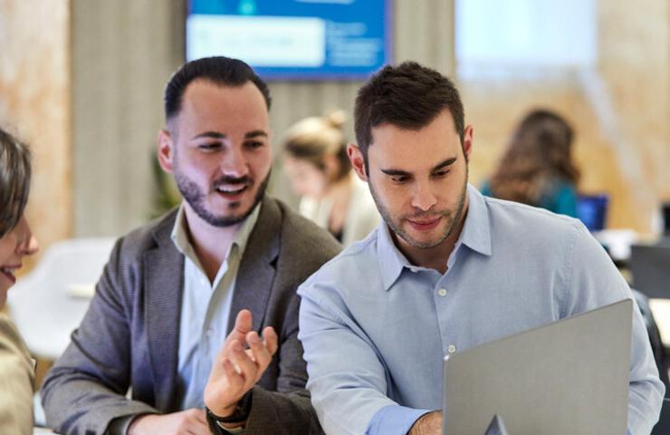 Three professionals discussing over a laptop in a modern office setting.