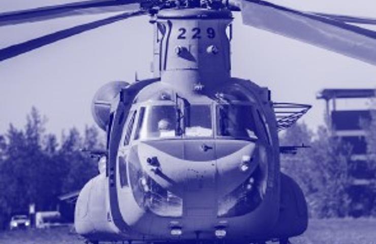 A blue-tinted photo of a military helicopter parked on a grassy field.