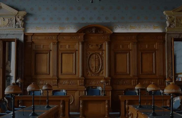 A panoramic view of a grand, classically designed courtroom with wooden furniture and large, ornate windows.