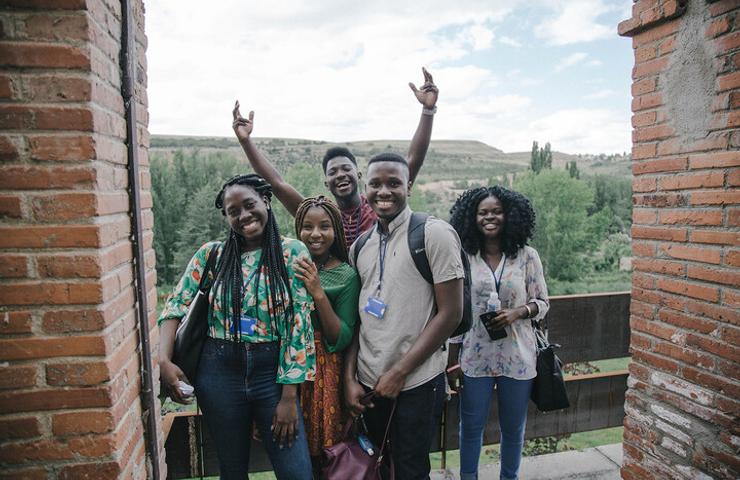A group of five smiling friends posing together outdoors with a scenic background.
