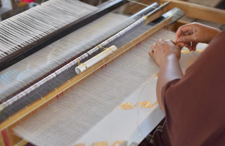 A person is weaving fabric on a traditional handloom, focusing on the intricate details of the pattern.