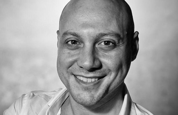 Black and white portrait of a smiling bald man wearing a white shirt.