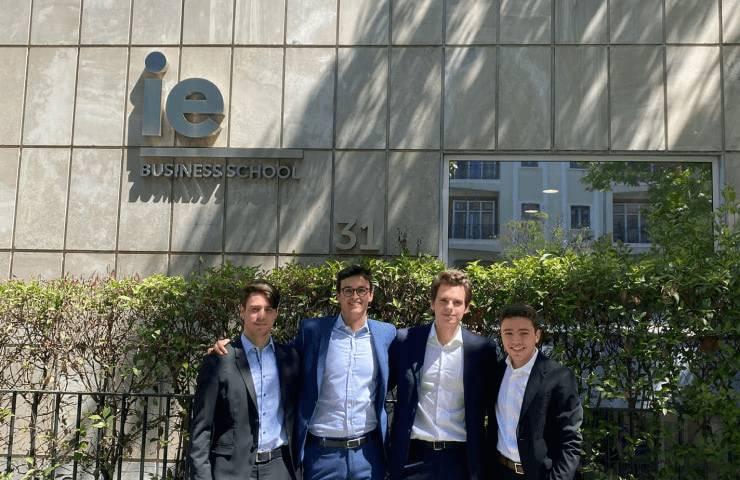 Four young men in business attire standing in front of the IE Business School building.