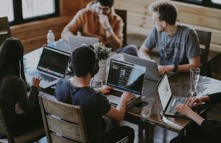 A group of people working on laptops at a wooden table in a cozy room.