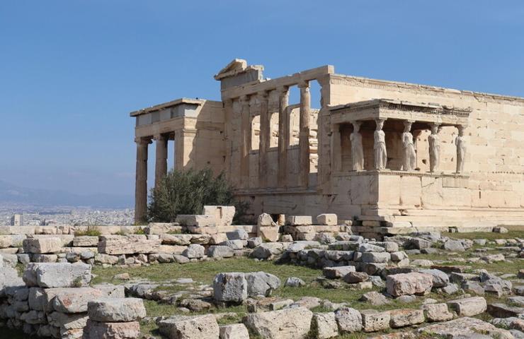 An ancient temple with iconic columns and a stone structure set against a clear blue sky.