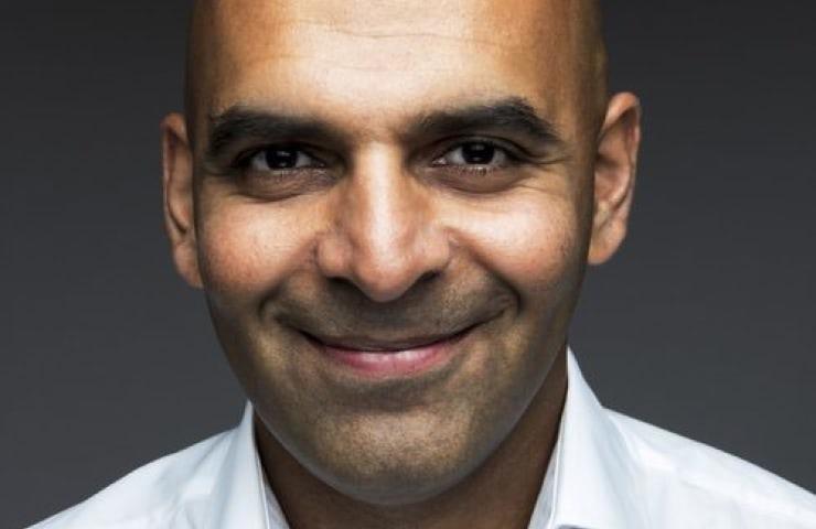 Portrait of a smiling bald man with dark skin against a dark background.