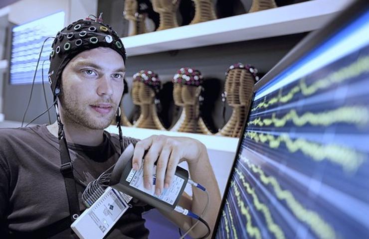 A man wearing an EEG cap observes brainwave readings on a monitor.