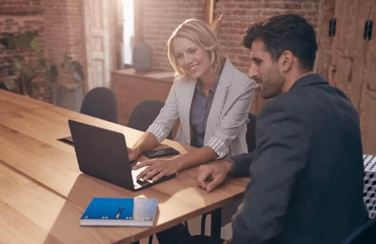 Two professionals are working together on a laptop in a well-lit office space.