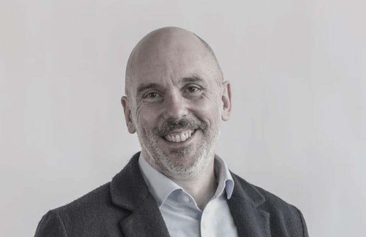 A portrait of a smiling bald man wearing a coat and a light blue shirt.