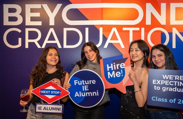 A group of four young women celebrating their graduation with signs at an event.