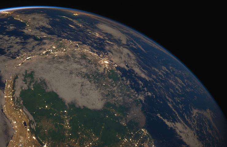 View of Earth from space showing continents and clouds illuminated by sunlight.