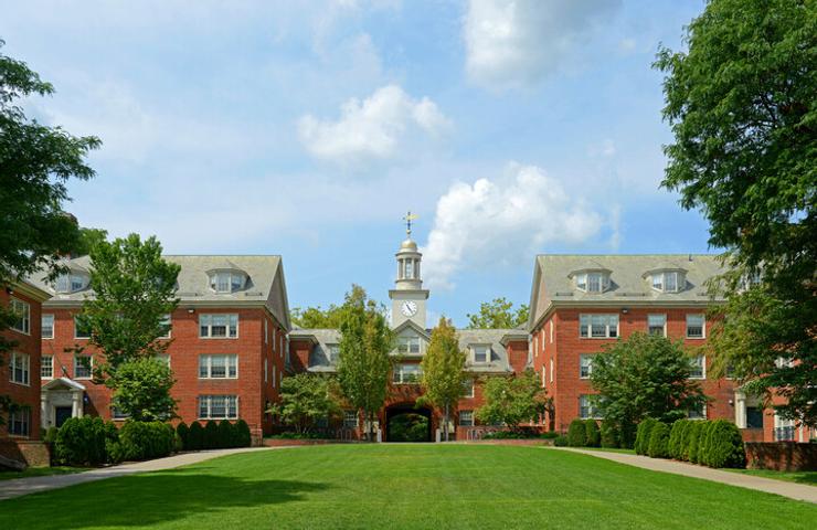 A scenic view of a college campus featuring brick buildings and a clock tower surrounded by greenery.