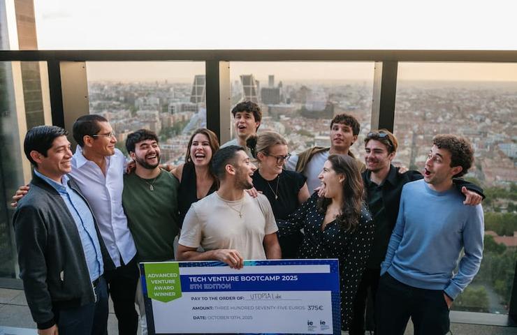 A group of young people celebrating while holding a large check with a city skyline in the background.