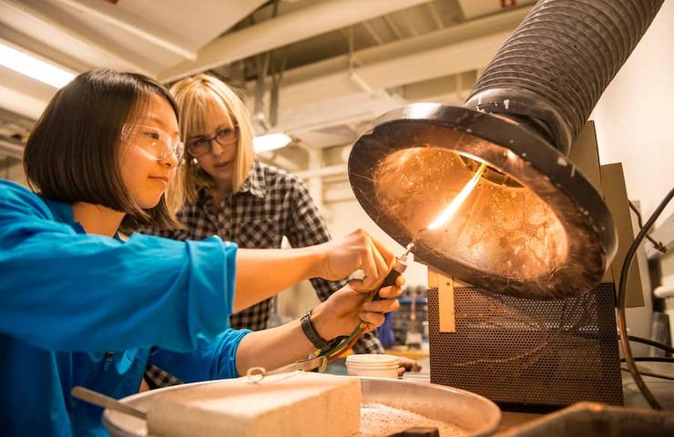 A student is using a torch while being supervised in a laboratory setting.