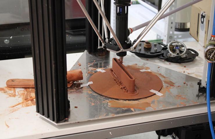 A 3D printer is creating a sculpture using clay material.