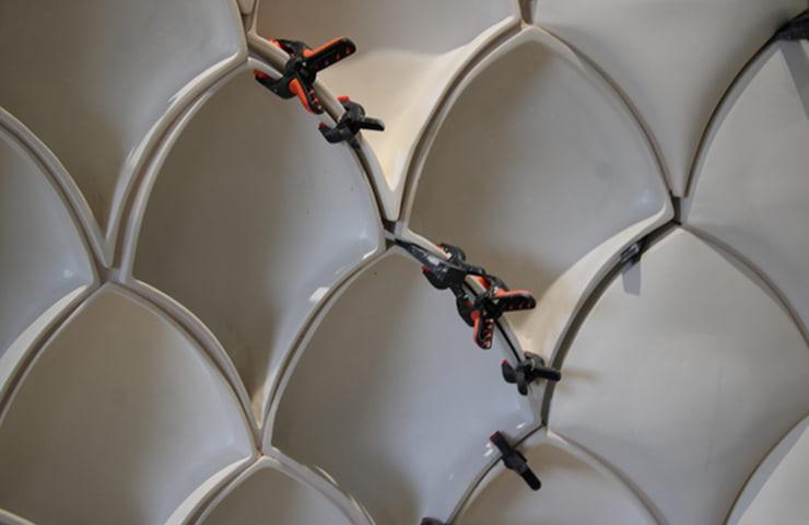 The image shows a close-up of a unique wall design featuring white, curved panels with black and red clamps securing some sections.