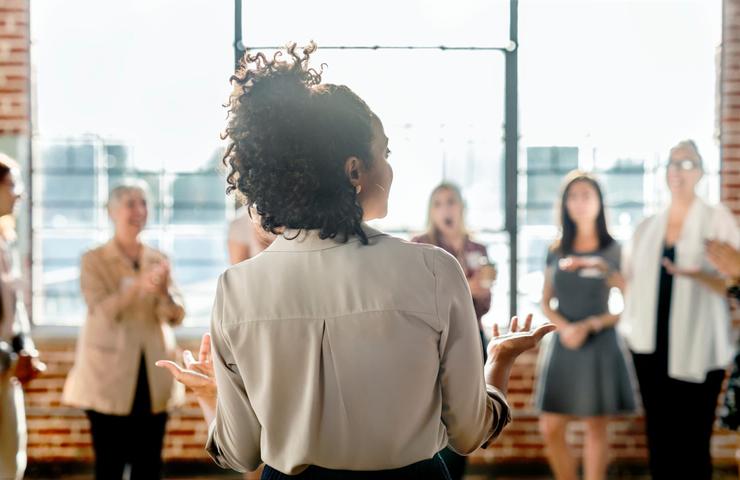 A woman is giving a presentation to a group of attentive colleagues in a brightly lit office space.