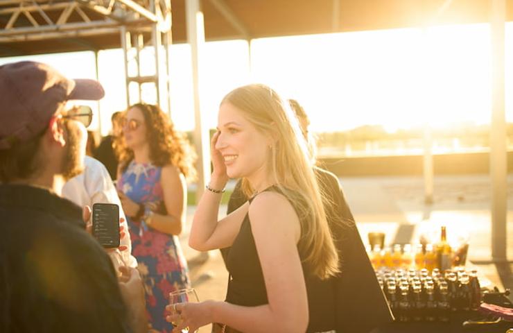 A woman smiling and engaging in a conversation at an outdoor party during sunset.