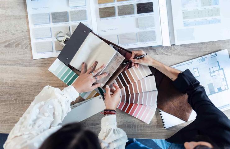 A top-down view of three people examining various fabric and color swatches on a table filled with design materials.