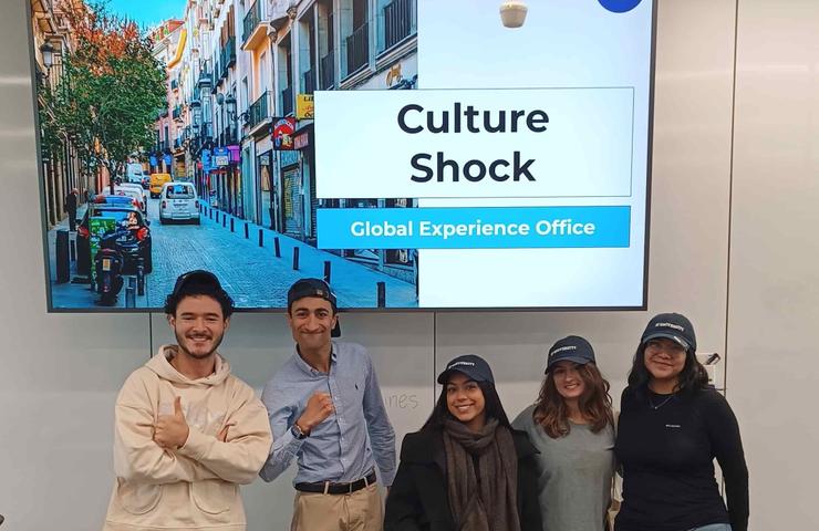 A group of four individuals posing happily in front of a presentation screen about culture shock.