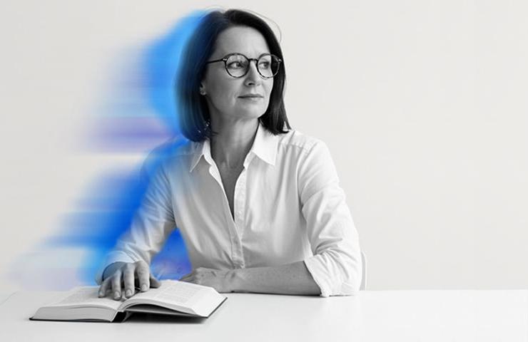 A woman with glasses sits at a table with a book, surrounded by a dynamic blue blur.