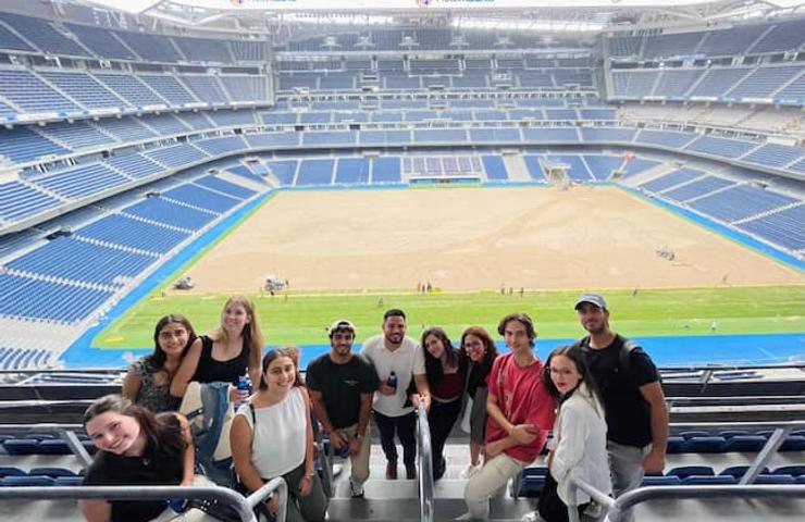 A group of people smiling and posing for a photo in a large, empty stadium with ongoing construction in the field.