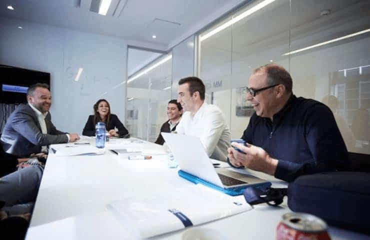 A group of professionals are seen engaging in a discussion around a conference table in a modern office setting.